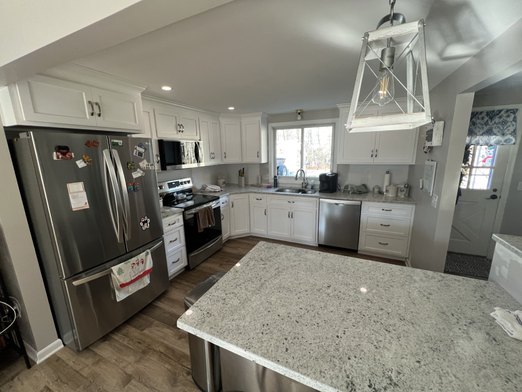 Bright modern kitchen with white cabinets, stainless steel appliances, granite island, and large window overlooking the outdoors Bright modern kitchen with white cabinets, stainless steel appliances, granite island, and large window overlooking the outdoors.