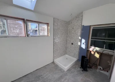 Empty bathroom during renovation featuring a shower base, hexagonal tiled wall, and multiple windows letting in natural light.