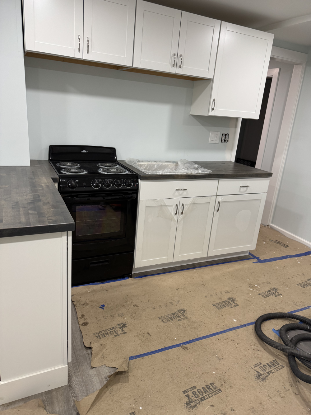 Newly remodeled kitchen with black stove, white cabinets, and a countertop. Floor covered with protective paper, indicating ongoing renovation