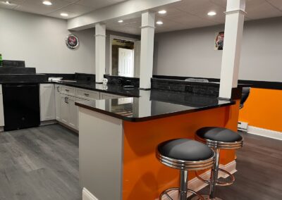 Modern kitchen area in a newly built in-law suite addition in Tolland, Connecticut, featuring black countertops, white cabinets, and orange accent walls.