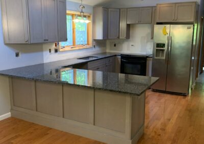 Modern kitchen in a newly built in-law suite addition in Vernon, CT, featuring granite countertops, wood flooring, and gray shaker cabinets.