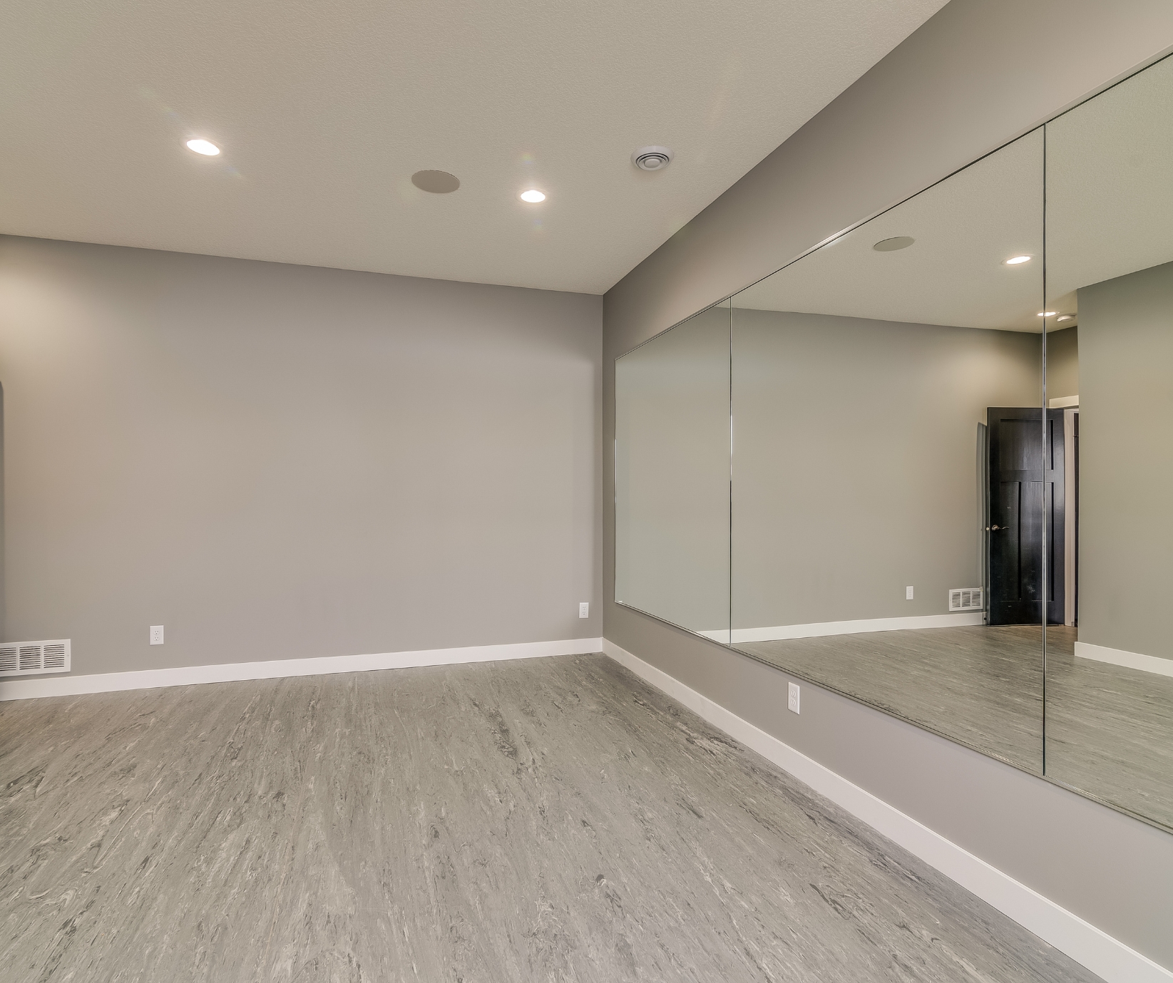 Finished basement in Tolland CT Finished basement in Tolland County CT with gray vinyl flooring, recessed lighting, and large wall mirror.